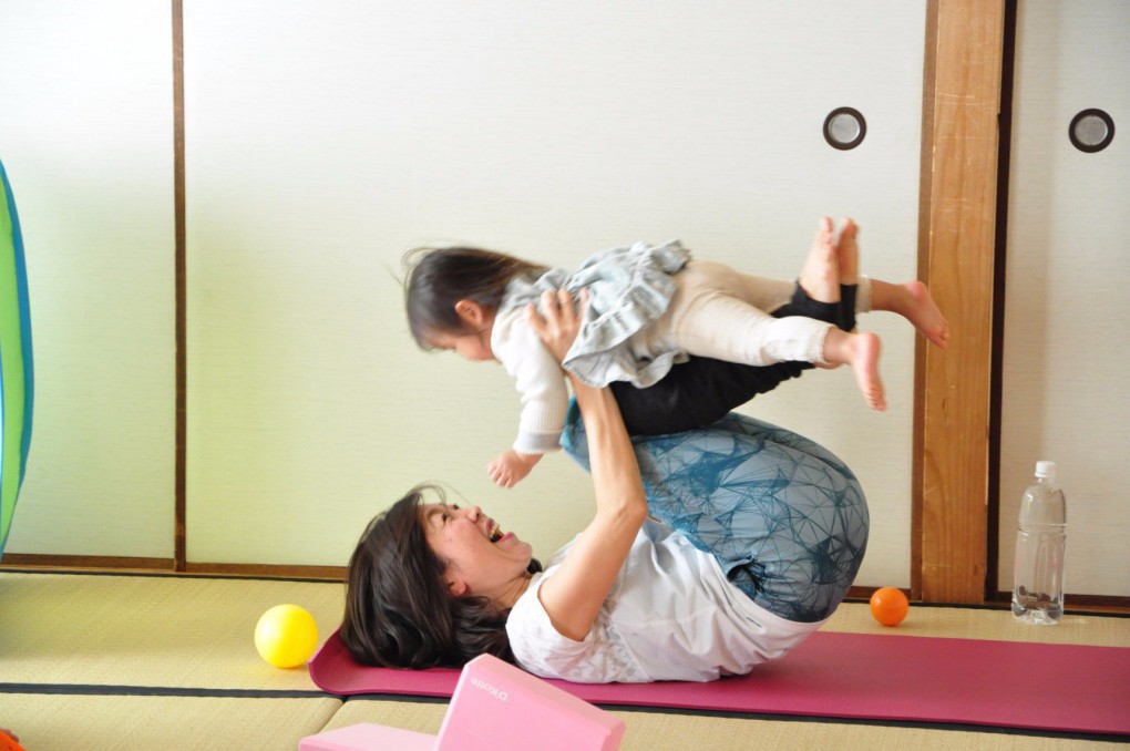 写真、参加者の赤ちゃんを抱き上げながらヨガをする藺牟田さん
