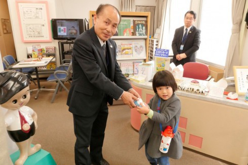 写真、あおいちゃんに貯金箱をプレゼントする館長の石山さん