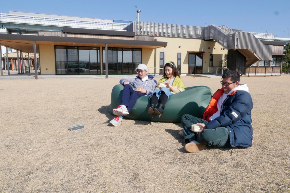 写真、芝生広場で昼食をとる三人