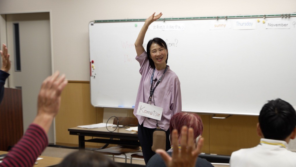 教室で手を挙げる英語の小松先生