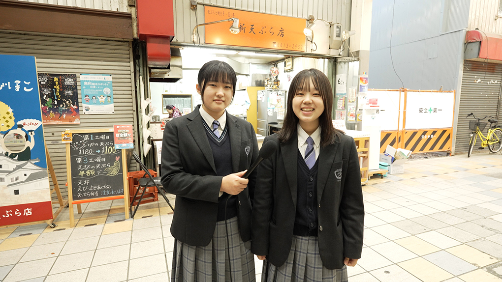 日新天ぷら店の前でレポートする高校生
