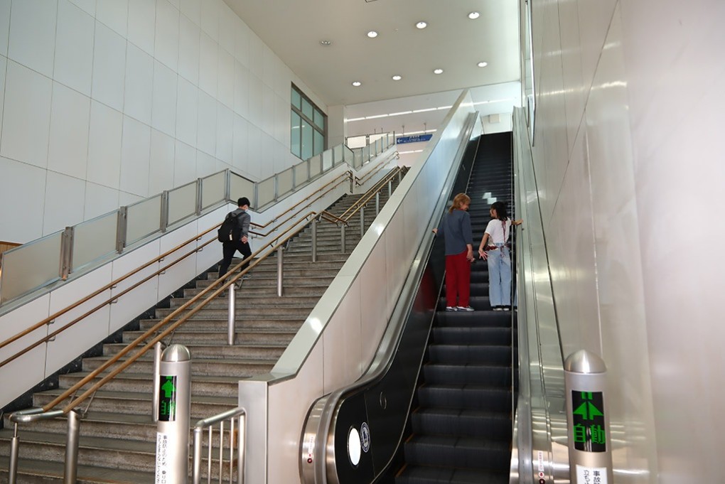 写真、駅のエスカレーターを上がる2人