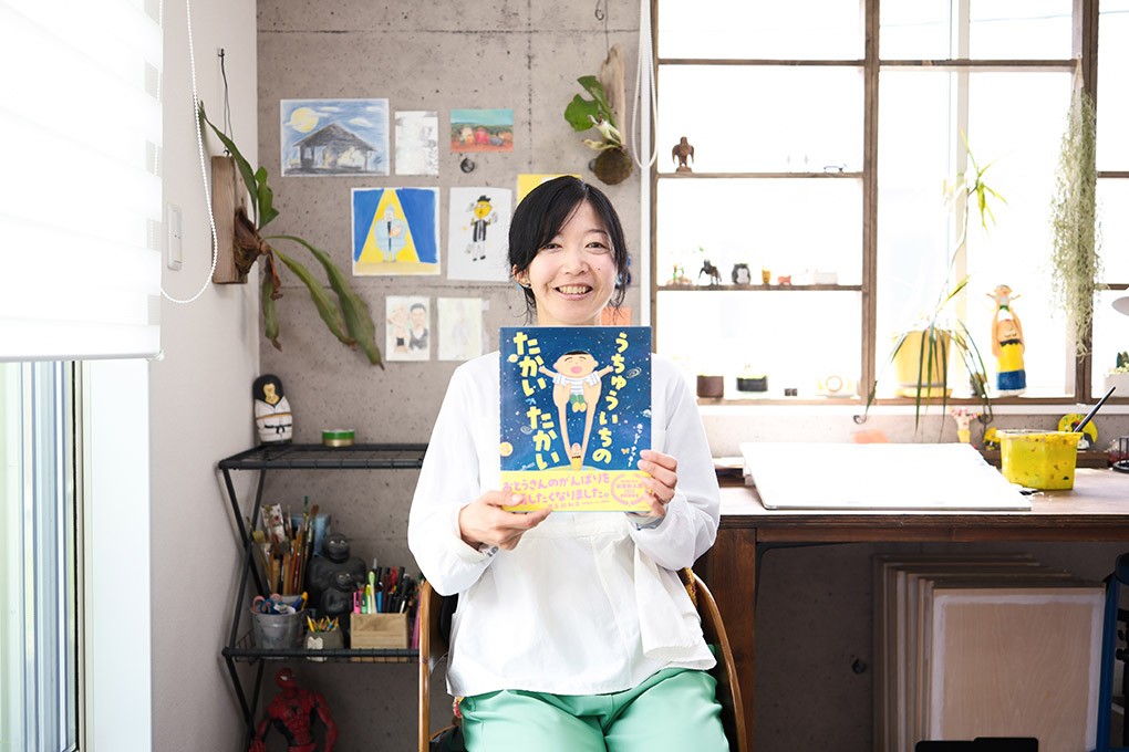 写真、創作机の前で絵本を持つ、ホッシー ナッキーさん