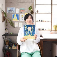 写真、創作机の前で絵本を持つ、ホッシー ナッキーさん