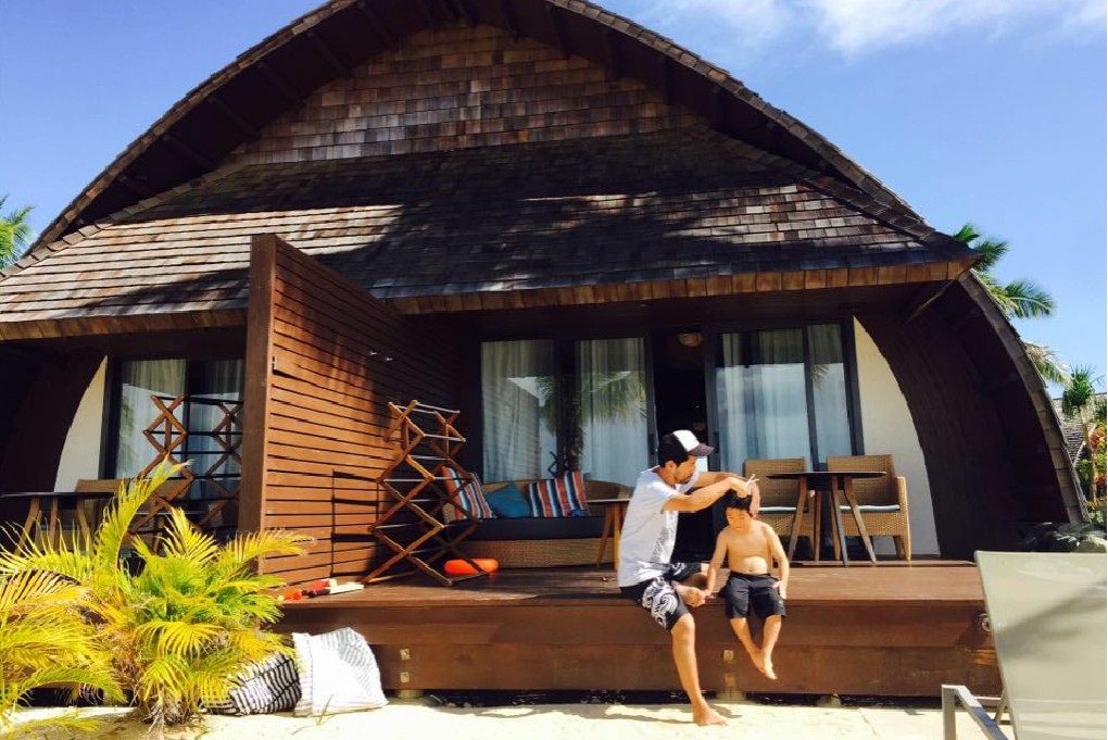 写真、フィジーのビーチ沿いでお子さんのヘアーカット中の永崎さん