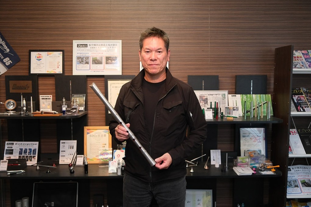 写真、金属製尺八「心妙」を手に持って立つ、金指博文さん