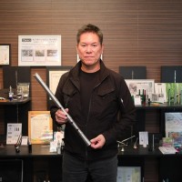 写真、金属製尺八「心妙」を手に持って立つ、金指博文さん