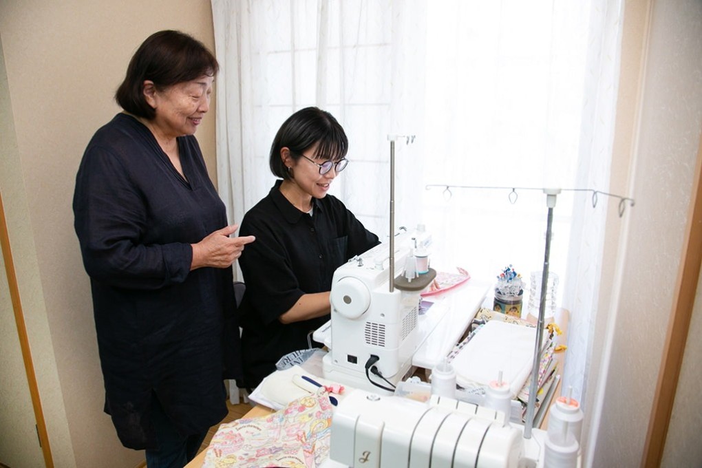 写真、井村さんの自宅で裁縫をしている筆者。