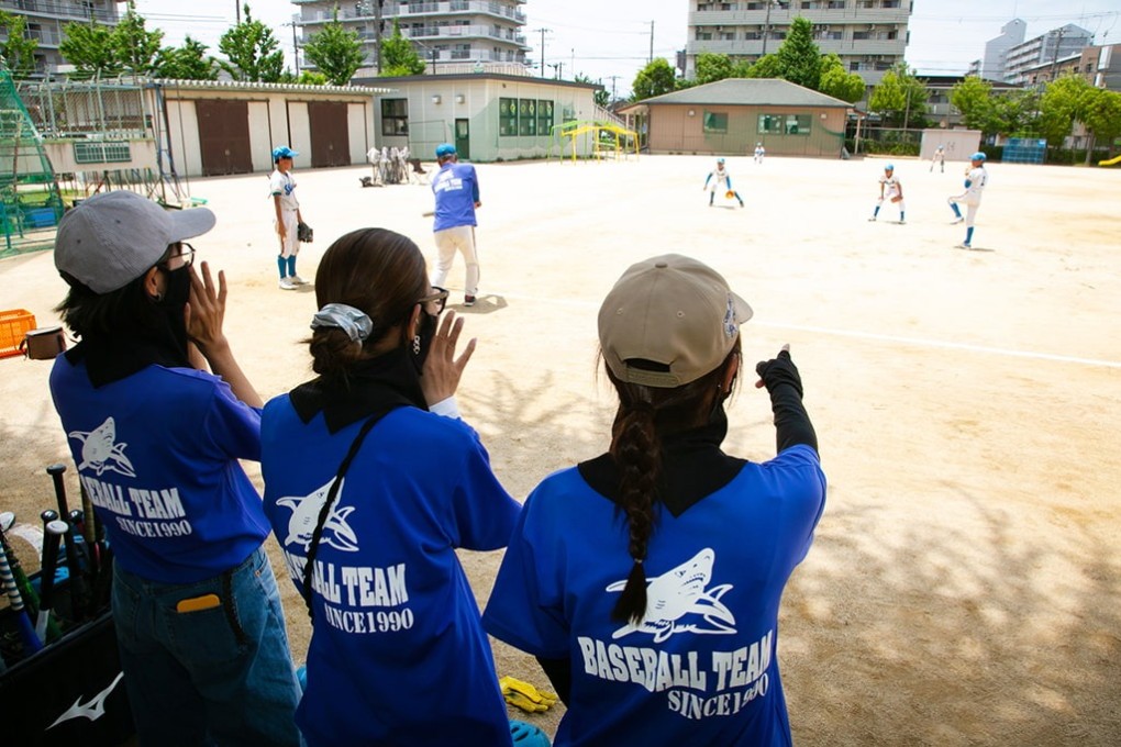 写真、野球をしているこどもたちを応援する保護者の皆さん。こどもたちが所属する野球チームのTシャツを着ている。