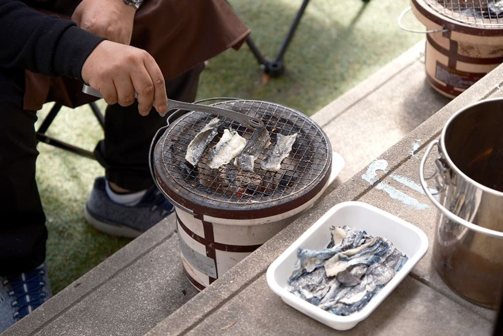 写真、庭で七輪を使い、利用者がクロダイの皮を香ばしく炙る作業