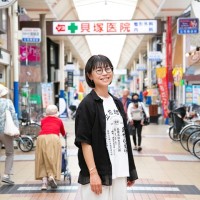 写真、立花商店街の中で笑顔の黒田さん。中に中田屋さんのオリジナルTシャツを着込んでいる。
