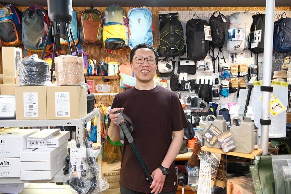 店内で山登り用のストックを持って笑う店主の糸田川さん